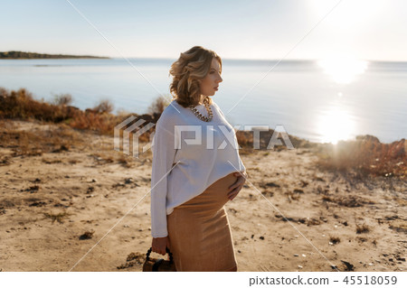 Pregnant woman walking near the river during the sunny weather Pregnant woman walking near the river during the sunny weather 45518059
