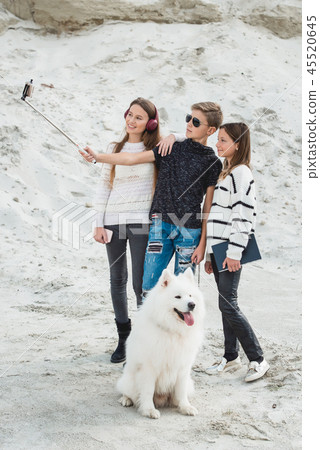 three friends with a doog breed samoyed makind selphie on a beach three friends with a doog breed samoyed makind selphie on a beach 45520645