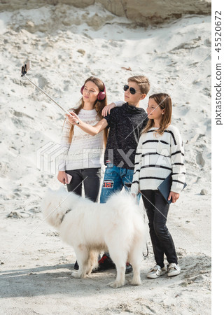 three friends with a doog breed samoyed makind selphie on a beach three friends with a doog breed samoyed makind selphie on a beach 45520672