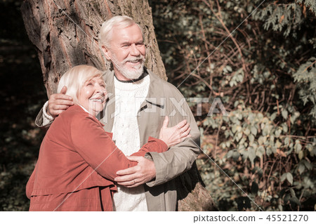 Delighted happy couple of pensioners standing near the tree 45521270
