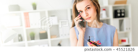 Beautiful Young girl in the office is standing near the table, holding glasses in her hand and Beautiful Young girl in the office is standing near the table, holding glasses in her hand and 45521826