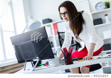 A young girl sat down on a Desk in the office and works with documents and a computer. A young girl sat down on a Desk in the office and works with documents and a computer. 45521837