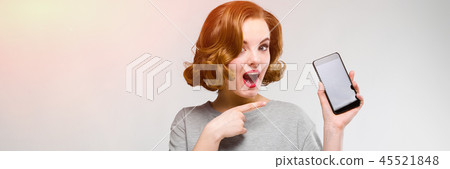 Charming young girl in a gray T-shirt on a gray background. A girl is holding a phone in her hand Charming young girl in a gray T-shirt on a gray background. A girl is holding a phone in her hand 45521848