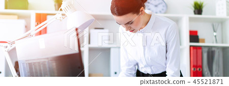 A young girl in the office is standing near the table, holding a pencil and a calculator in her hand 45521871