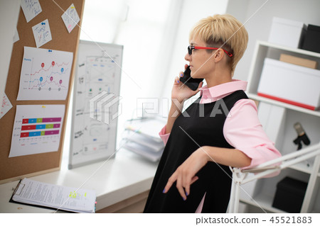 A young girl standing in the office and holding a phone. A young girl standing in the office and holding a phone. 45521883