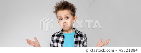 A handsome boy in a plaid shirt, blue shirt and jeans stands on a gray background. The boy spread A handsome boy in a plaid shirt, blue shirt and jeans stands on a gray background. The boy spread 45521884
