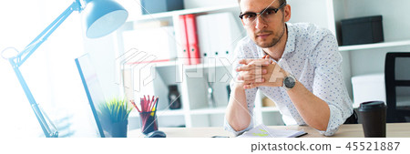 A young man in glasses stands near a table in the office. A young man in glasses stands near a table in the office. 45521887