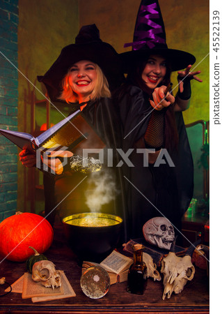Picture of smiling witches in black hats with book and magic cauldron at table with pumpkin and 45522139