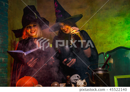 Portrait of smiling two witches in black hats reading book at table with pumpkin and skulls Portrait of smiling two witches in black hats reading book at table with pumpkin and skulls 45522140
