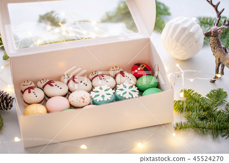 Variety of sweet macaroons in white box. The branches of spruce on bokeh background. Modern european 45524270