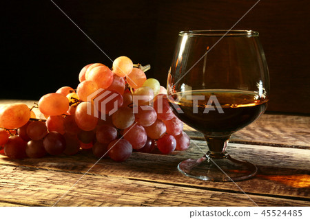 Cognac or Brandy in a glass and fresh grapes, still life in rustic style, vintage wooden background Cognac or Brandy in a glass and fresh grapes, still life in rustic style, vintage wooden background 45524485