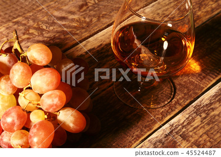 Cognac or Brandy in a glass and fresh grapes, still life in rustic style, vintage wooden background Cognac or Brandy in a glass and fresh grapes, still life in rustic style, vintage wooden background 45524487
