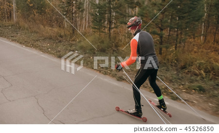 Training an athlete on the roller skaters. Biathlon ride on the roller skis with ski poles, in the 45526850