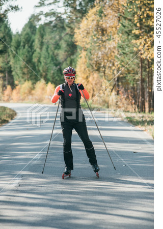 Training an athlete on the roller skaters. Biathlon ride on the roller skis with ski poles, in the 45527026