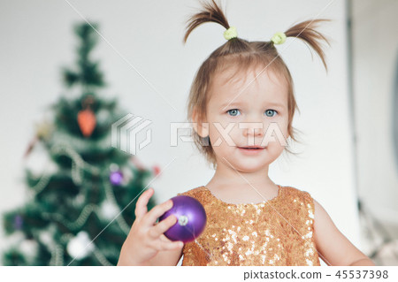 a little girl in a dress adorns the Christmas tree a little girl in a dress adorns the Christmas tree 45537398