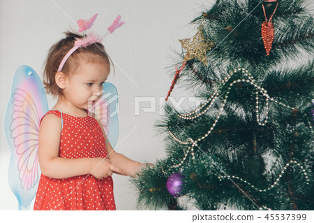 a little girl in a dress adorns the Christmas tree a little girl in a dress adorns the Christmas tree 45537399