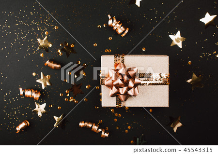 Gift box with golden bow on black background with decoration and sparkles. 45543315