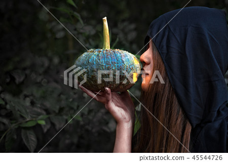 Female wizard kissing pumpkin lantern. Female costume in black c Female wizard kissing pumpkin lantern. Female costume in black c 45544726