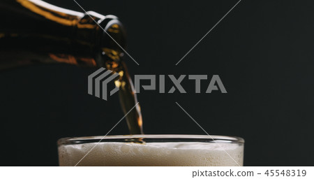 Closeup pour dark beer from brown bottle into glass on black background Closeup pour dark beer from brown bottle into glass on black background 45548319