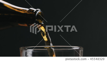 Closeup pour dark beer from brown bottle into glass on black background 45548320