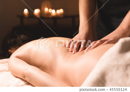 Close-up male hands doing healing massage with oil to a young girl in a dark cosmetology office 45550124
