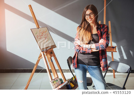 Pretty Pretty Girl artist paints on canvas painting on the easel. Studio black background. Long hair 45553120