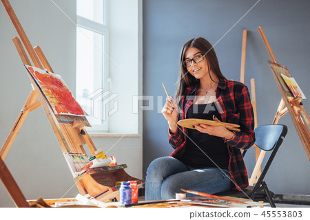 Dark-haired artist holding a brush in his hand and draws a picture on canvas. Thinks that draw on Dark-haired artist holding a brush in his hand and draws a picture on canvas. Thinks that draw on 45553803