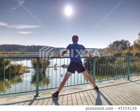 Tall sportsman warming up muscles legs before run Tall sportsman warming up muscles legs before run 45554139