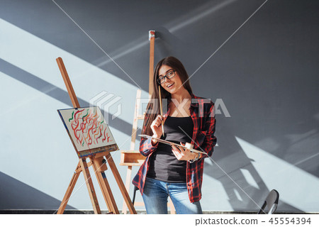 Creative pensive painter girl paints a colorful picture on canvas with oil colors in workshop. 45554394