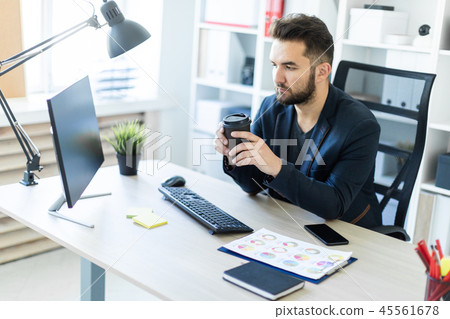 A young man working in the office at the computer and holding a glass of coffee. A young man working in the office at the computer and holding a glass of coffee. 45561678