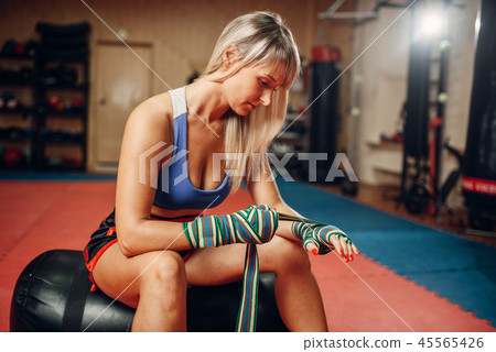 Female kickboxer sitting on punching bag in gym Female kickboxer sitting on punching bag in gym 45565426