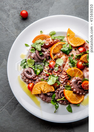 Whole octopus salad with orange, tomatoes and cress salad on white plate. Top view Whole octopus salad with orange, tomatoes and cress salad on white plate. Top view 45569850