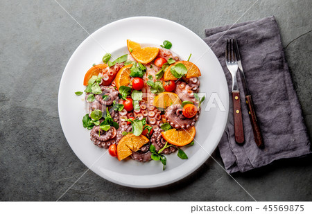 Whole octopus salad with orange, tomatoes and cress salad on white plate. Top view Whole octopus salad with orange, tomatoes and cress salad on white plate. Top view 45569875