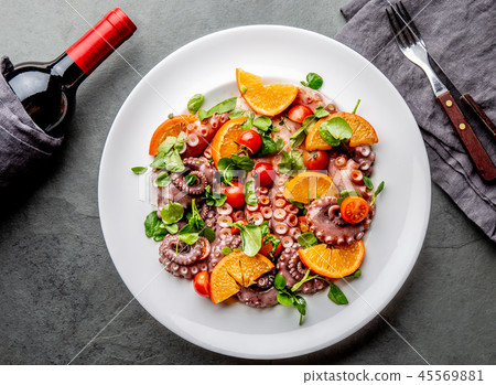 Whole octopus salad with orange, tomatoes and cress salad on white plate. Top view 45569881