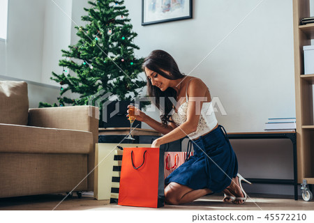 Woman siting by the christmas tree and taking a present out of shopping bag Woman siting by the christmas tree and taking a present out of shopping bag 45572210