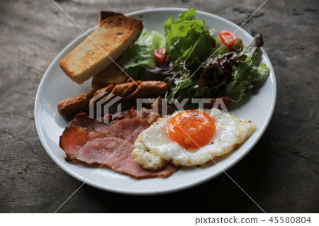 English breakfast fried egg, ham,sausage, bacon,salad and toast on wood background in mystic light English breakfast fried egg, ham,sausage, bacon,salad and toast on wood background in mystic light 45580804