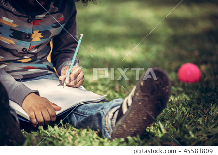 Little child writing on a notebook in the park. 45581809