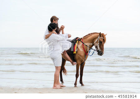 Young couple goes horse riding on tropical beach. 45581914