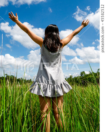 Young woman on green grass spreading arms to sky. 45582512