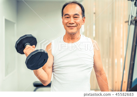 Senior man lifting dumbbell in fitness gym. 45582683