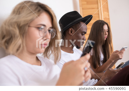 Multiracial group of friends are sitting on the bed and usie smartphone. 45590091