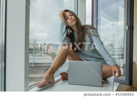Beautiful young woman sitting on the windowsill with a laptop. 45590993