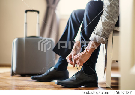 Midsection of businessman on a business trip sitting in a hotel room, tying shoelaces. 45602187