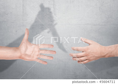 Two male hands getting close for a handshake with a shadow of one hand holding a knife on a concrete 45604711