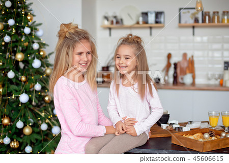 Two sisters in their pajamas in the kitchen preparing breakfast laugh. Christmas and New Year Two sisters in their pajamas in the kitchen preparing breakfast laugh. Christmas and New Year 45606615