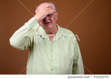Overweight senior man wearing eyeglasses against brown backgroun 45609970