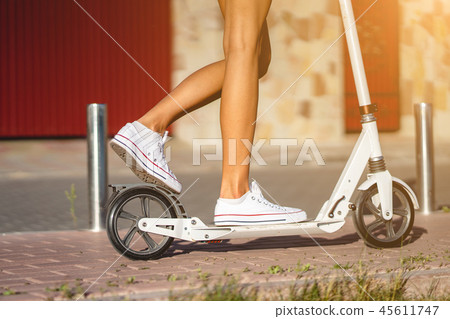 Beautiful girl riding a scooter down the street Beautiful girl riding a scooter down the street 45611747