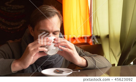 Young Man Wearing a Scarf Drinking Tea and Smiling in a cafe. Young Man Wearing a Scarf Drinking Tea and Smiling in a cafe. 45623092