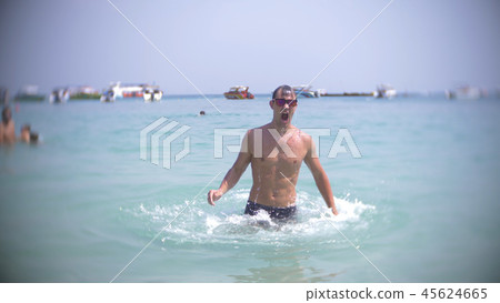 a young man dives into the sea wearing sunglasses. emerges and smiles 45624665