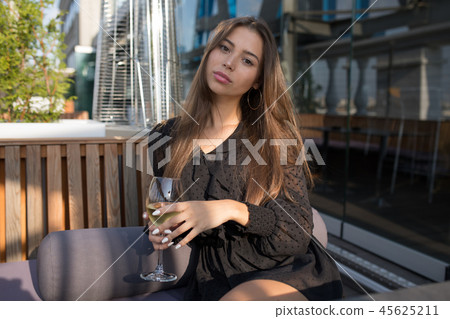 Young woman sitting on the terrace of a restaurant with a glass of wine. 45625211